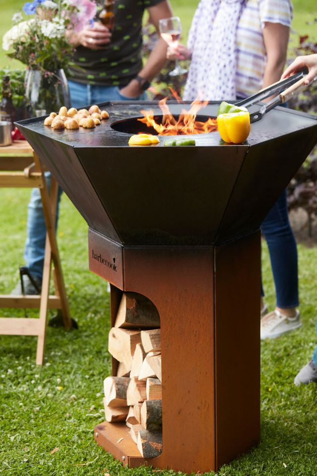 Barbecue brasero deux en un Nestor ; structure en acier corten et deux plaques de cuisson amovibles en acier carbone de 91 cm de diamètre, pieds en plastique pour éviter les tâches de rouille sur les sols ; espace de rangement intégré pour le bois et les outils ; jusqu'à 14 couverts ; compatible avec les accessoires du Dynamic Centre ; 101x91 cm de diamètre ; 799 euros pour la version en acier corten, existe aussi en acier galvanisé à 899 euros.