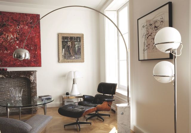 Dans le salon, le célèbre lampadaire "Arco" imaginé en 1962 par les frères Castiglioni illumine une table basse en verre et alu achetée à Saint-Ouen à la galerie Artefactdesign. La "Lounge Chair" des Eames a été rapportée des États-Unis. Derrière, lampe "Pipistrello" de Gae Aurenti (Martinelli Luce) et tableau de Jean Puy. À côté, peinture de Ramon Hernandez et cheminée Louis XV en marbre rose. Au premier plan, lampadaire sur pied acheté chez un antiquaire.